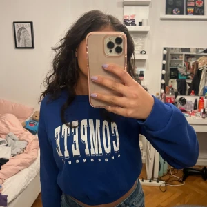 Blå sweatshirt med tryck - Säljer en blå sweatshirt med stort vitt tryck på framsidan. Tröjan har långa ärmar och en avslappnad passform, perfekt för en casual look. 