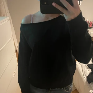 Svart offshoulder tröja - Säljer en stilren svart offshoulder tröja. Perfekt för en avslappnad look med jeans. Tröjan har långa ärmar och en lös passform som ger en bekväm känsla.