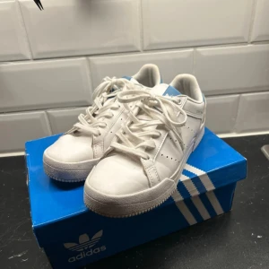 Vita Adidas sneakers - Säljer ett par vita Adidas sneakers med blå detaljer. Skorna har tecken på användning men är inte förstörda. Se bild💓