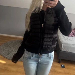 Svart dunväst från Moncler - Snygg svart dunväst från Moncler med dragkedja framtill. Västen har en quiltad design och är perfekt för lager-på-lager under kyligare dagar. Den har en normal passform och är ett stilrent tillskott till garderoben.