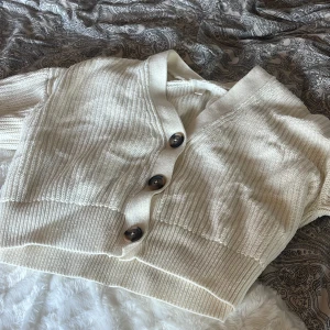 Vit kofta - Säljer en mysig vit/ljusbeige stickad kofta från H&M med stora knappar framtill. Koftan har en v-ringad design och ribbade detaljer vid ärmslut och nederkant. Perfekt för kyliga dagar! Storlek 175, dvs storlek S-M🤍