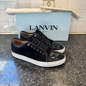 Lanvins uk 9 - Snygga svarta sneakers från Lanvin med en kombination av mocka och glansigt material på tån. Skorna har snörning och en vit sula som ger en stilren kontrast. Perfekta för en trendig look. Uk 9 passar 43/44 priser går att diskutera vid snabb affär allt og ingår vid köpet går att köpa utan og till billigare pris.