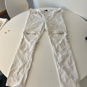 Vita byxor med dragkedjor - Snygga vita byxor från HM med dragkedjor på låren. De har en straight passform och är perfekta för en stilren look. Byxorna har en midwaist design och är tillverkade i ett bekvämt material.