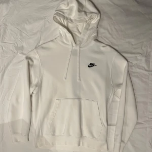 Vit hoodie från Nike - Säljer en stilren vit hoodie från Nike med klassisk logga på bröstet. Den har en stor ficka framtill och justerbar huva med dragsko. Perfekt för en avslappnad look.