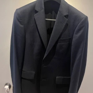 TIGER OF SWEDEN helt ny och oanvänd skräddarsydd kavaj. Mörklblå och randig. NYPRIS 7499.  - Snygg mörkblå kavaj från Tiger of Sweden med diskreta ränder. Klassisk design med två knappar framtill och fickor. Perfekt för en stilren look. 