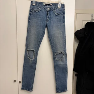 Blå jeans med slitna knän - Snygga blå jeans med slitna detaljer vid knäna. De har en tight passform och klassisk femficksdesign. Perfekta för en avslappnad stil.