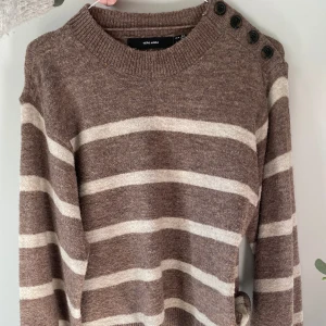 Brunrandig tröja från Vero Moda - Säljer denna randiga tröjan från Vero Moda med knappar på ena axeln. Tröjan har långa ärmar och är perfekt för kyligare dagar. Den är mjuk och bekväm❤️ 