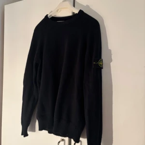 Svart tröja från Stone Island - Säljer en stilren svart tröja från Stone Island med deras ikoniska märke på ärmen. Tröjan har långa ärmar och en klassisk rund halsringning. Perfekt för en avslappnad och trendig look.