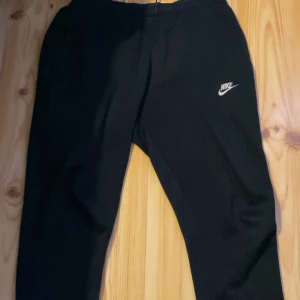 Svarta mjukisbyxor från Nike - Säljer ett par svarta mjukisbyxor från Nike med elastisk midja och det klassiska Nike-loggan på benet. Perfekta för en avslappnad stil.  OBS: Finns en liten skada på höger ficka 