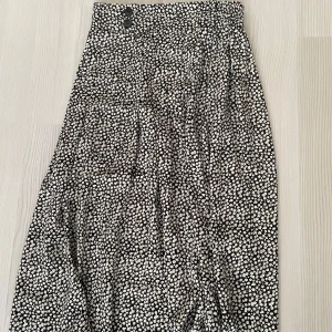 Svartvit blommig kjol - Snygg svartvit blommig kjol med knappar i midjan. Perfekt för en stilren look. Kjolen har en bekväm passform och är lätt att matcha med olika toppar.