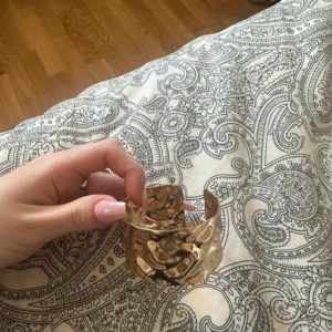 Brett guldarmband - Säljer ett brett guldarmband med en vågig design. Armbandet har en öppen baksida för justerbar passform. Det är från SHEIN och är endast använd en gång. 