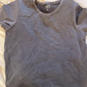 Grå tränings t-shirt från New Apparel - Säljer en stilren grå t-shirt från New Apparel i storlek XS. T-shirten har en diskret broderad detalj på bröstet och är tillverkad i ett mjukt material. Perfekt för en avslappnad look. Skriv via intresse och fler bilder!⭐️