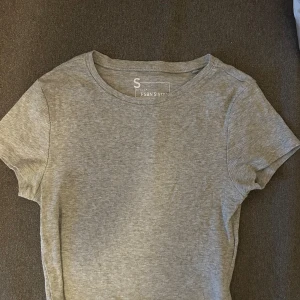 Grå ribbad top - Säljer en stilren grå ribbad top. Den har en klassisk rund hals och korta ärmar, perfekt för en avslappnad look. 