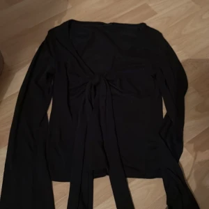 Svart långärmad topp med knyt - Snygg svart långärmad topp med knyt framtill. Perfekt för en stilren look och kan matchas med olika outfits. Passar bra till både vardag och fest.