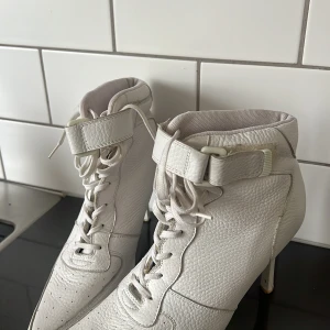 Vita klackskor med snörning från Dallas ,USA  - Snygga vita klackskor med snörning och kardborreband. Skorna har en spetsig tå och är tillverkade i syntetmaterial. Perfekta för att ge en stilren look.