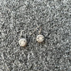 Örhängen med kapsylmotiv - Unika örhängen med kapsylmotiv i silverfärg. De har en rund form och hängande design, vilket ger en cool och avslappnad stil. Perfekta för den som vill ha något annorlunda i smyckesamlingen.