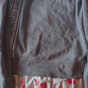 Grå tröja från Calvin Klein Jeans - Säljer en stilren grå tröja från Calvin Klein Jeans. Tröjan har en klassisk design med märkets logga längs sidan. Perfekt för en avslappnad look.