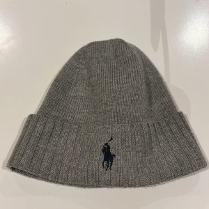 Grå stickad mössa från Ralph Lauren - Snygg grå stickad mössa från Ralph Lauren med broderad logga. Använd några få gånger, ser ut som ny!
