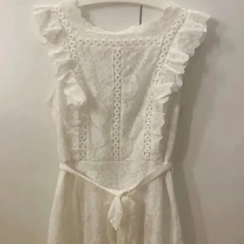 Säljer en vacker vit spetsklänning från DM med volangdetaljer och knytband i midjan. Klänningen är ärmlös och har en romantisk känsla, perfekt för sommarens festligheter. 💫. Mekot.