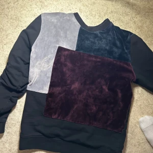 Flerfärgad tröja från Le Vichy - Säljer en unik flerfärgad tröja från Le Vichy med patchwork-design i svart, grått, blått och vinrött. Tröjan har långa ärmar och ett broderat emblem på ärmen. Perfekt för dig som vill sticka ut med stil! Storlek S och nypris ligger på mellan 1000-1300, mitt pris 450