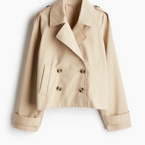 Beige kort trenchcoat - Snygg beige trenchcoat som endast är testad, lappen kvar. Perfekt för vår och höst! Tryck på köp nu