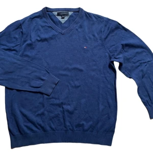 Blå v-ringad tröja från Tommy Hilfiger - Säljer en stilren blå v-ringad tröja från Tommy Hilfiger. Tröjan har långa ärmar och en liten logotyp på bröstet. Perfekt för en avslappnad men snygg look.