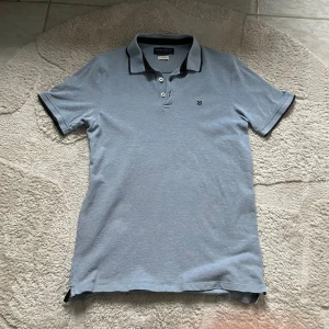 Ljusblå pikétröja från Jack & Jones - Säljer en stilren ljusblå pikétröja från Jack & Jones. Tröjan har en klassisk krage med knappar och ett diskret broderat emblem på bröstet. Perfekt för en avslappnad men ändå snygg look.
