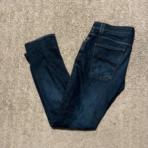 Nudie jeans  - Snygga mörkblå jeans med en cool slitning på ena benet. Storlek 30/31. Fråga om modell.