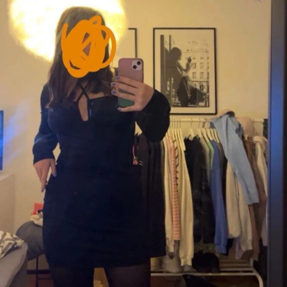 Snygg svart klänning med lång ärm och knytning framtill. Perfekt för en stilren look med en touch av elegans. Klänningen har en åtsittande passform som framhäver figuren.. Mekot.