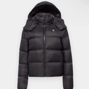 Svart dunjacka från Calvin Klein - Snygg svart dunjacka från Calvin Klein med huva och dragkedja. Jackan har en pufferdesign och är perfekt för kyligare väder. Den har långa ärmar och en diskret logga på bröstet. Perfekt för att hålla dig varm och stilren. Köpt för 1800 . Pris kan diskuteras 