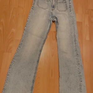 Ljusblå jeans med bootcut Divided - Säljer ett par ljusblå jeans med bootcut-stil. De har en klassisk femficksdesign och är högmidjade för en bekväm passform. Perfekta för en avslappnad look.