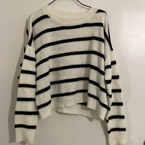 Vit och svart randig stickad tröja - Säljer en mysig vit stickad tröja med svarta ränder. Tröjan har en avslappnad passform och långa ärmar, perfekt för kyligare dagar. Den är både stilren och bekväm, ett måste i garderoben!