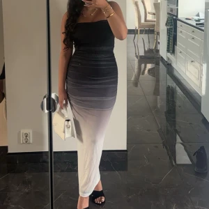 Vacker kvälls klänning - Snygg axelbandslös klänning i svart och vit med en gradvis övergång mellan färgerna. Klänningen har en tight passform som framhäver figuren och är perfekt för en elegant kväll. Den långa längden ger en sofistikerad look.