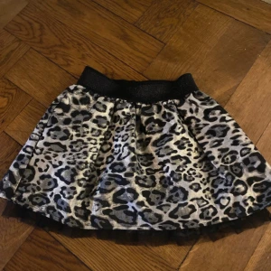 Leopardmönstrad kjol från Name It - Snygg leopardmönstrad kjol från Name It i svart och grått. Kjolen har en elastisk midja för bekväm passform och är perfekt för att ge en cool look. Passar bra för små fashionistas som gillar att sticka ut. 🐆✨