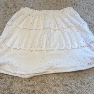 Vit kjol från Ardene i New York  - Vit kjol från Ardene med volangdetaljer och broderade mönster. Perfekt för en somrig look. Den har en elastisk midja för bekväm passform.