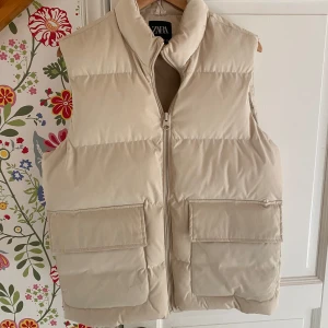 Dunväst från Zara - Säljer en snygg beige dunväst från Zara i storlek S men fungerar perfekt för M också. Perfekt för höst och vår när du vill hålla dig varm men ändå se stilren ut. 