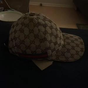 Mönstrad keps från Gucci - Säljer en snygg keps från Gucci i storlek XS. Den har ett klassiskt mönster i beige och brunt med märkets logga. Perfekt för att ge din outfit en lyxig touch. Kepsen är i mycket bra skick och passar perfekt för både vardag och fest.