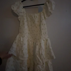 Blommig klänning från H&M Divided - Söt blommig klänning från H&M Divided i storlek L. Klänningen har en ljus bas med små blommor och volanger. Aldrig använd pga för stor stolek 