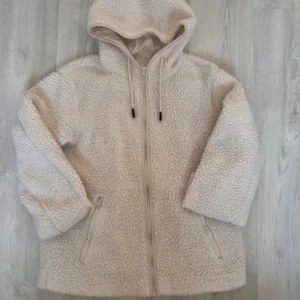 Beige teddyjacka med huva - Mysig beige teddyjacka i damstorlek XS. Perfekt för kyliga höst- och vinterdagar. Jackan har en dragkedja framtill och en praktisk huva. Den är långärmad och har en skön, fluffig textur som håller dig varm och bekväm.