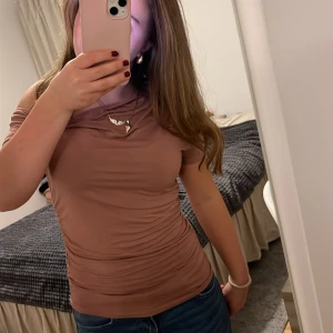 Brun ärmlös topp - Säljer en snygg brun ärmlös topp i ett mjukt och stretchigt material. Perfekt för sommardagar eller att ha under en kavaj. Toppen har en enkel design med en liten detalj vid halsen. Passar både till vardags och fest!