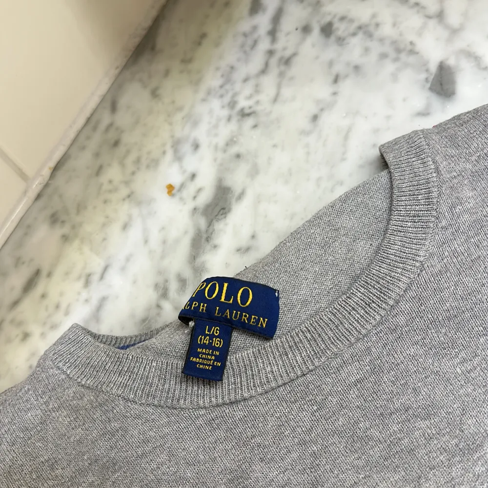 Säljer en stilren grå tröja från Polo Ralph Lauren i storlek L. Tröjan är i mycket bra skick och har en klassisk design med rund hals och det ikoniska blå logotypbroderiet på bröstet. Perfekt för både vardag och lite finare tillfällen. Passar bra till jeans eller chinos!😇🌟. Tröjor & Koftor.