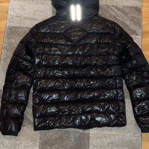 Svart pufferjacka från Canada Goose - Säljer en snygg svart pufferjacka från Canada Goose. Den är quiltad och har en dragkedja framtill. Perfekt för kalla dagar med sin varma och stiliga design. Jackan är i mycket bra skick och kommer med originalförpackning. Passar perfekt för höst och vinter!