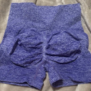 Blå träningsshorts - Säljer ett par blå träningsshorts i mycket bra skick. De är högmidjade och har en tight passform som ger bra stöd under träningen. Materialet är stretchigt och bekvämt, perfekt för intensiva träningspass. Shortsen har en snygg scrunch. 