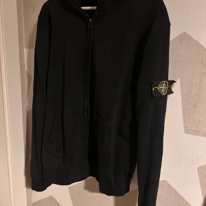 Stone Island zip up - Säljer en svart zip up från Stone Island i mycket bra skick. Den har en dragkedja framtill och en ikonisk logga på ärmen. Perfekt för höst och vår, med en normal passform och långärmade ärmar. Grym för både vardag och fest! Skriv innan du köper!