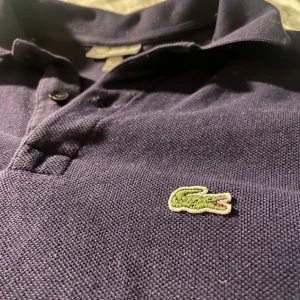 Mörkblå pikétröja från Lacoste - Säljer en klassisk mörkblå pikétröja från Lacoste i mycket bra skick. Tröjan är väldigt stilren och passar till olika tillfällen, hör av er vid frågor, nypris ca 700kr säljer för 199