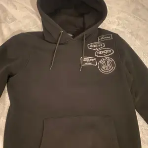 Säljer en svart hoodie från Mercier i storlek M. Den har flera coola patches med Mercier-loggan på bröstet och texten 'Product of Mercier' på ryggen. Perfekt för en avslappnad stil och passar till alla tillfällen. Grymt skön och stilren!