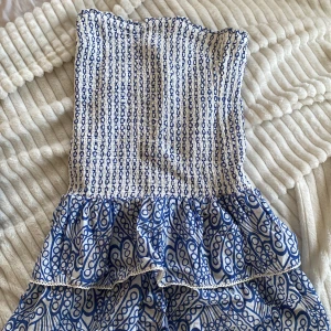 Blåvit klänning från Gina Tricot - Säljer en superfin blåvit klänning från Gina Tricot i storlek 158/164. Klänningen har ett elastiskt smockliv och volangdetaljer i nederkant. Perfekt för sommardagar eller en avslappnad fest. Mönstret är unikt och ger en härlig bohemisk känsla. 🦋