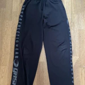 Svarta träningsbyxor från GASP - Säljer ett par svarta träningsbyxor från GASP Athletic Wear. De har en loose passform med snörning i midjan för bästa komfort. Perfekta för gymmet eller andra träningsaktiviteter. Byxorna har tryck längs benen som ger en cool look.