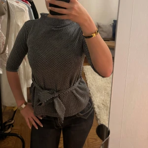 Topp - Svartvit topp med mönster. Den har trekvartsärmar och en knytning i midjan. Xs men sitter mer som S.
