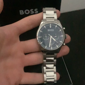 Silverfärgad klocka från Boss - Säljer en stilren och elegant klocka från Boss i silverfärg. Klockan har en blå urtavla med flera små urtavlor och datumvisning. Armbandet är i rostfritt stål och ger en lyxig känsla. Perfekt för både vardag och fest! Kommer i originalförpackning. Pris billigare vid snabb affär eller upphämtning av klockan